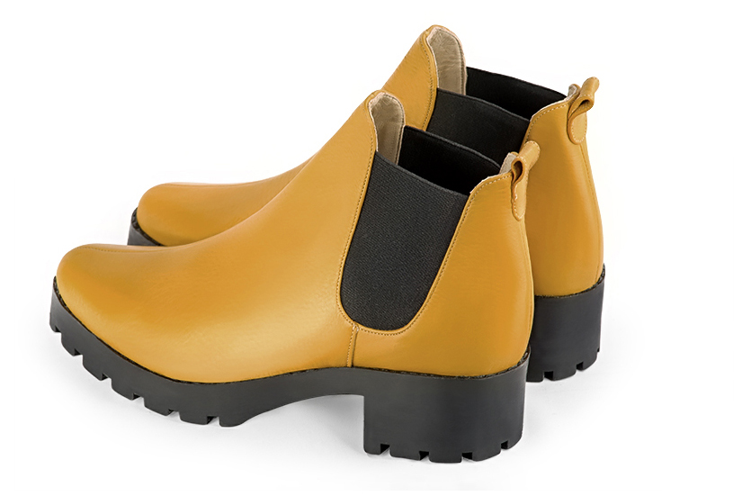 Mustard yellow and matt black women's ankle boots, with elastics. Round toe. Low rubber soles. Rear view - Florence KOOIJMAN